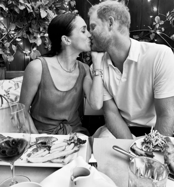 Meghan Markle and Prince Harry share a kiss in a black-and-white Instagram photo, with a table set with food in front of them.